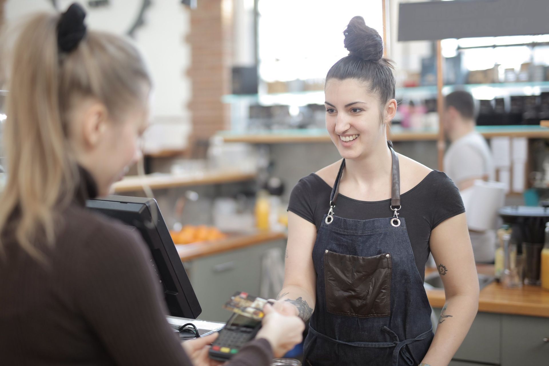 Barista smiles while handing a card to a customer across a café counter.