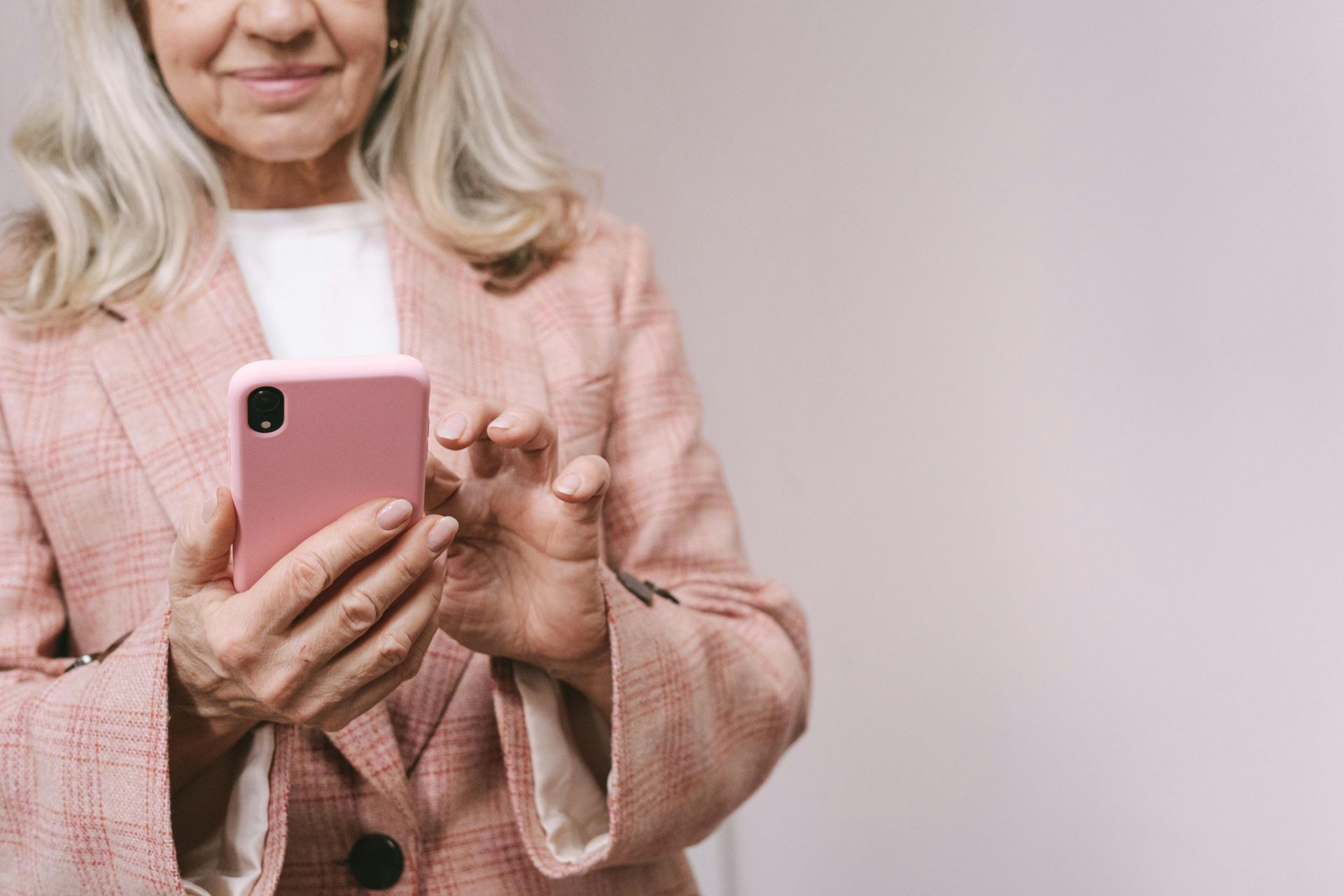 Woman holding a pink smartphone in a light pink sweater against a plain background