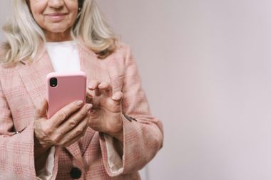 Woman holding a pink smartphone in a light pink sweater against a plain background