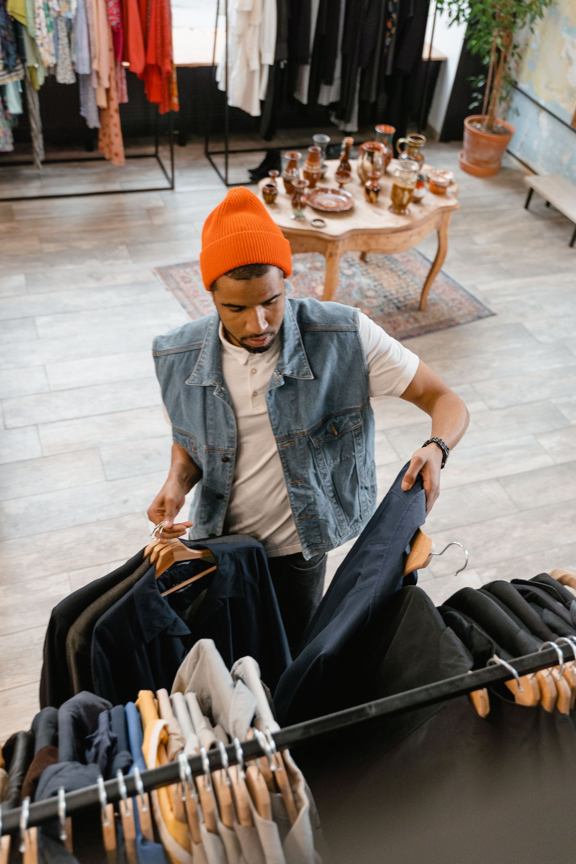 Person in orange beanie browsing clothes on racks in a boutique, with dresses in the background
