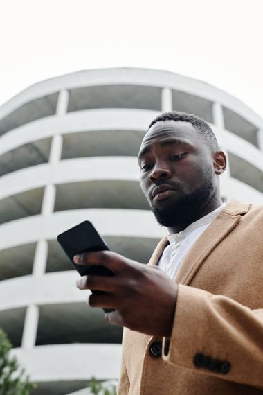 Man in tan coat looking at a smartphone in front of a curved modern building