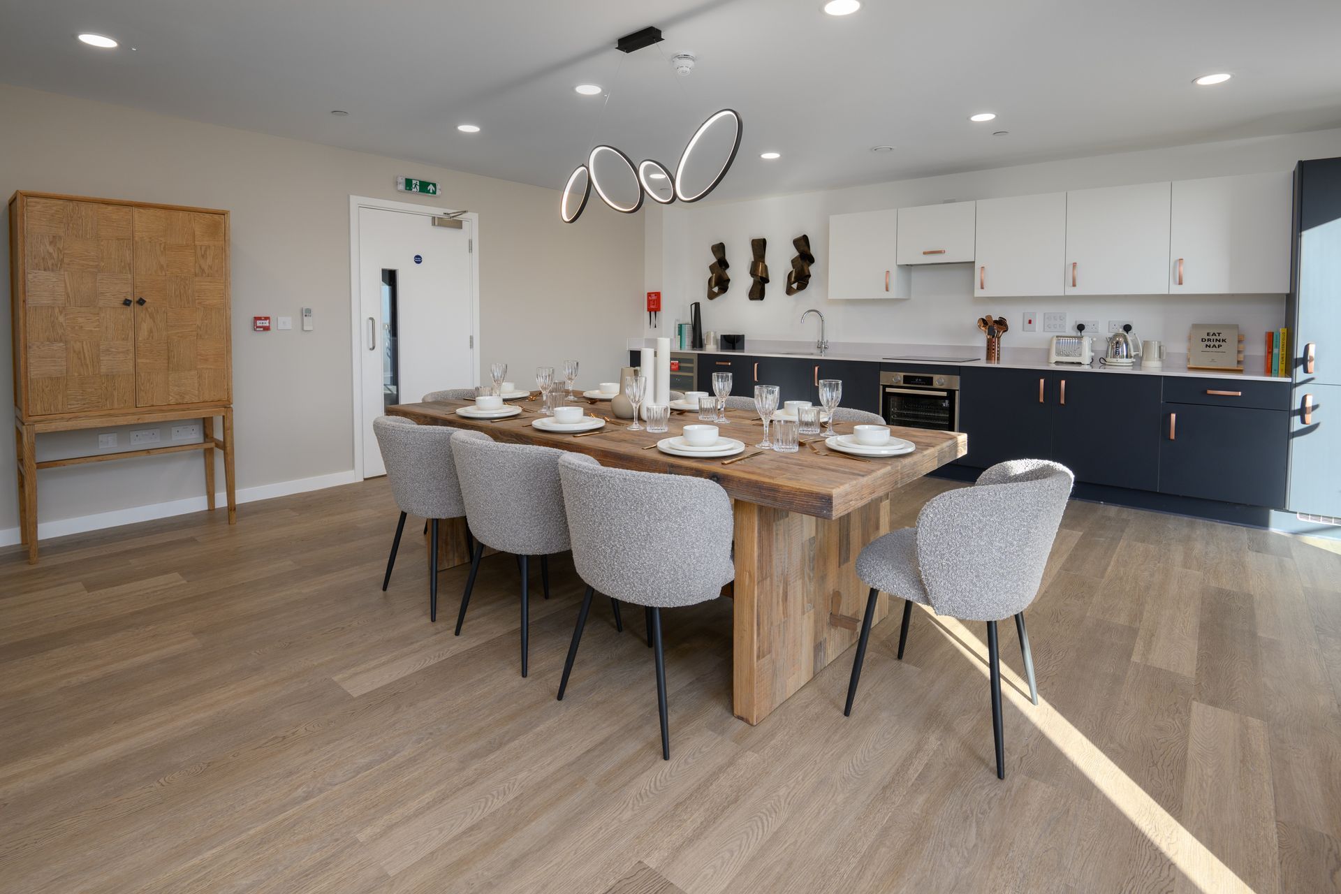 A dining room with a long wooden table and chairs and a kitchen at Walton Court.