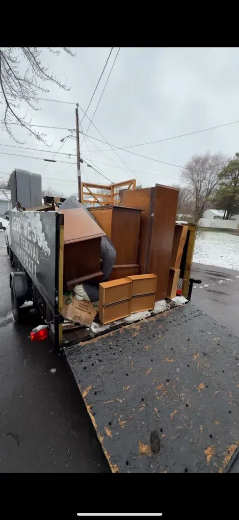 A truck bed filled with furniture and debris. Exterior setting with a cloudy sky and snow on the ground.