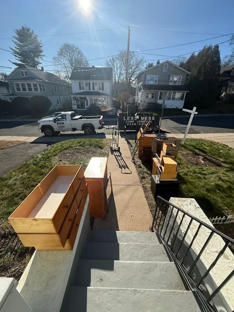 Furniture being moved from a house with stairs. Boxes, dresser drawers, truck parked on street, sunny day.
