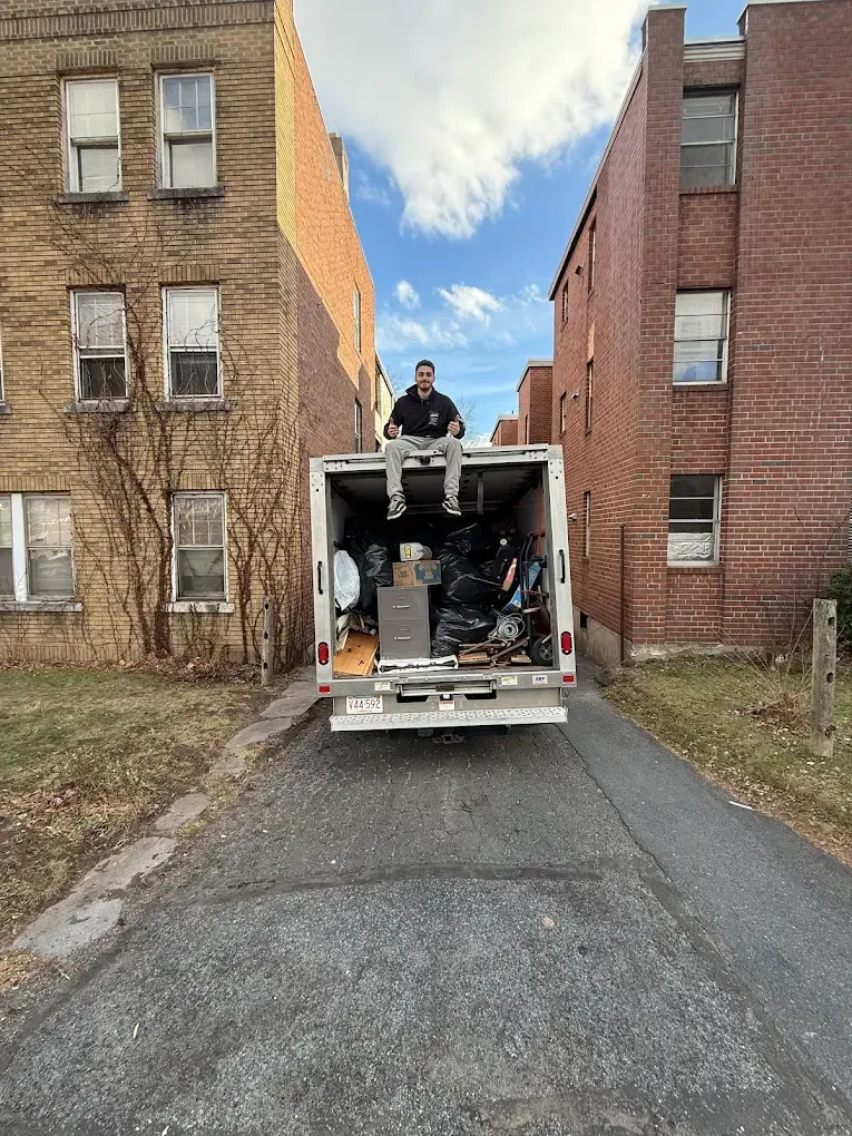 Man sitting on the roof of a moving truck parked between two brick buildings.