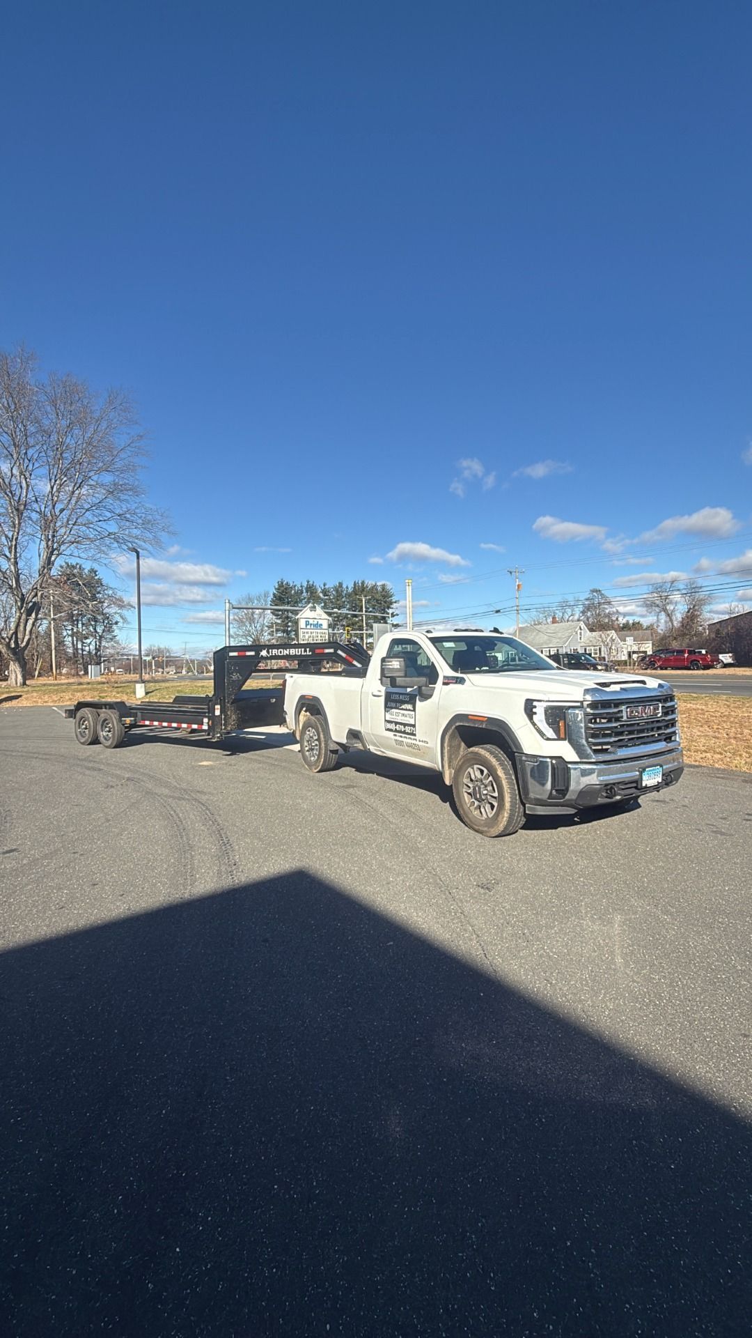 White pickup truck with trailer parked on gravel, under a blue sky.