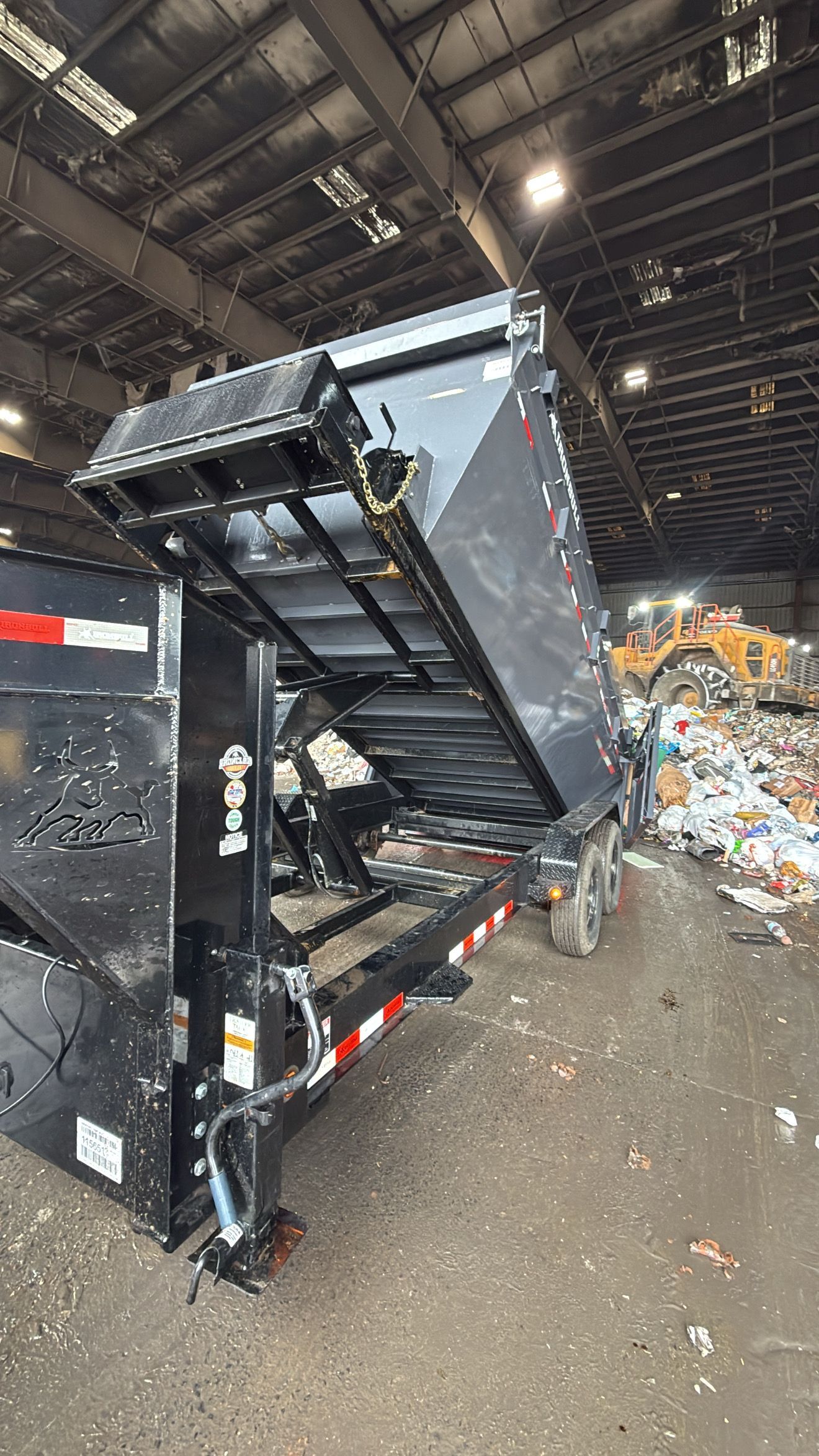 Black dump trailer raising its bed, inside a waste sorting facility.
