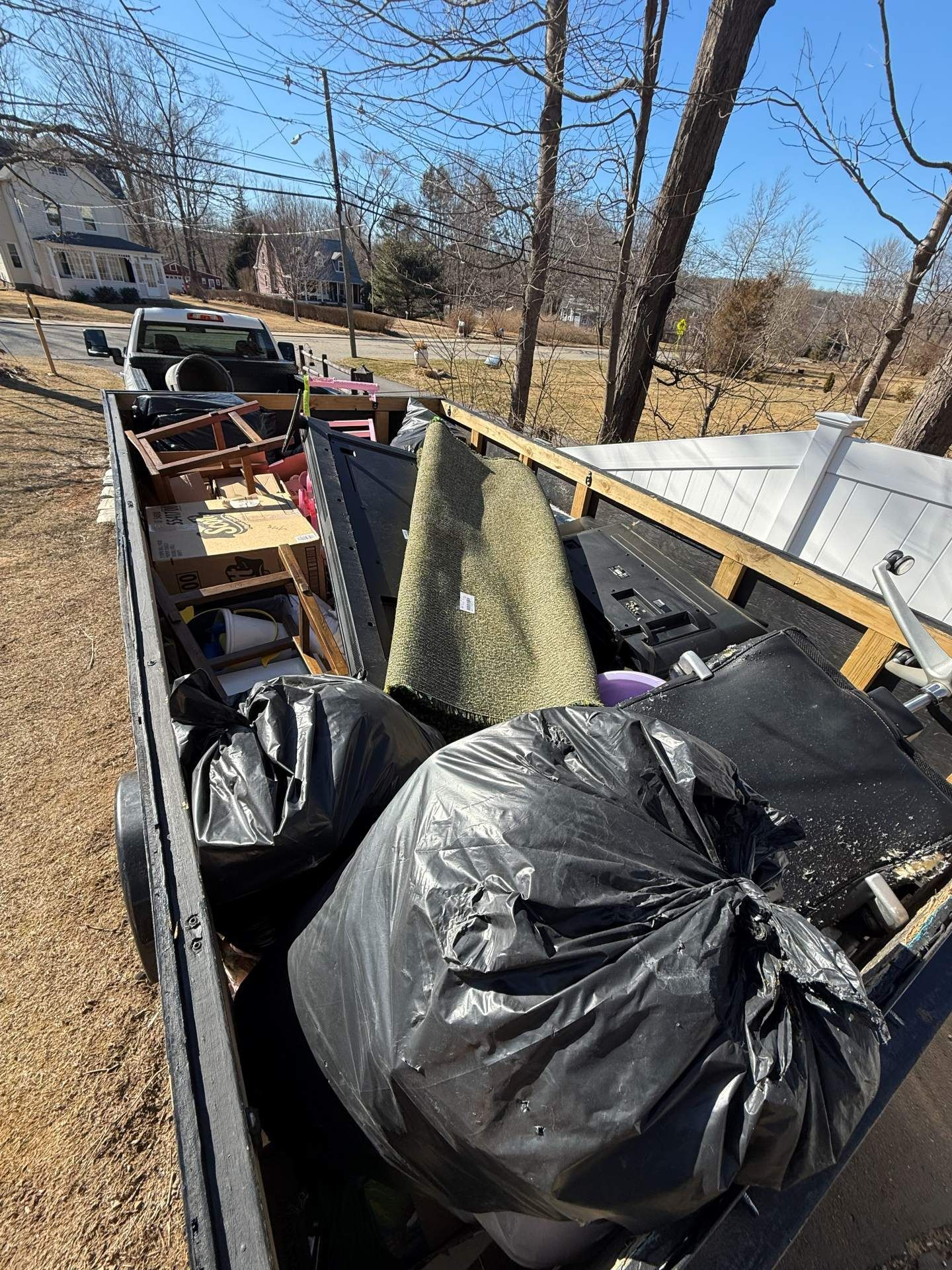 A truck bed filled with trash bags, a rug, and various debris outdoors on a sunny day.