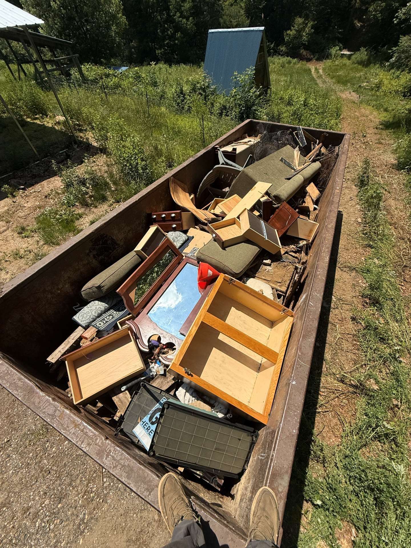 A metal dumpster overflowing with discarded furniture and debris in an outdoor setting.