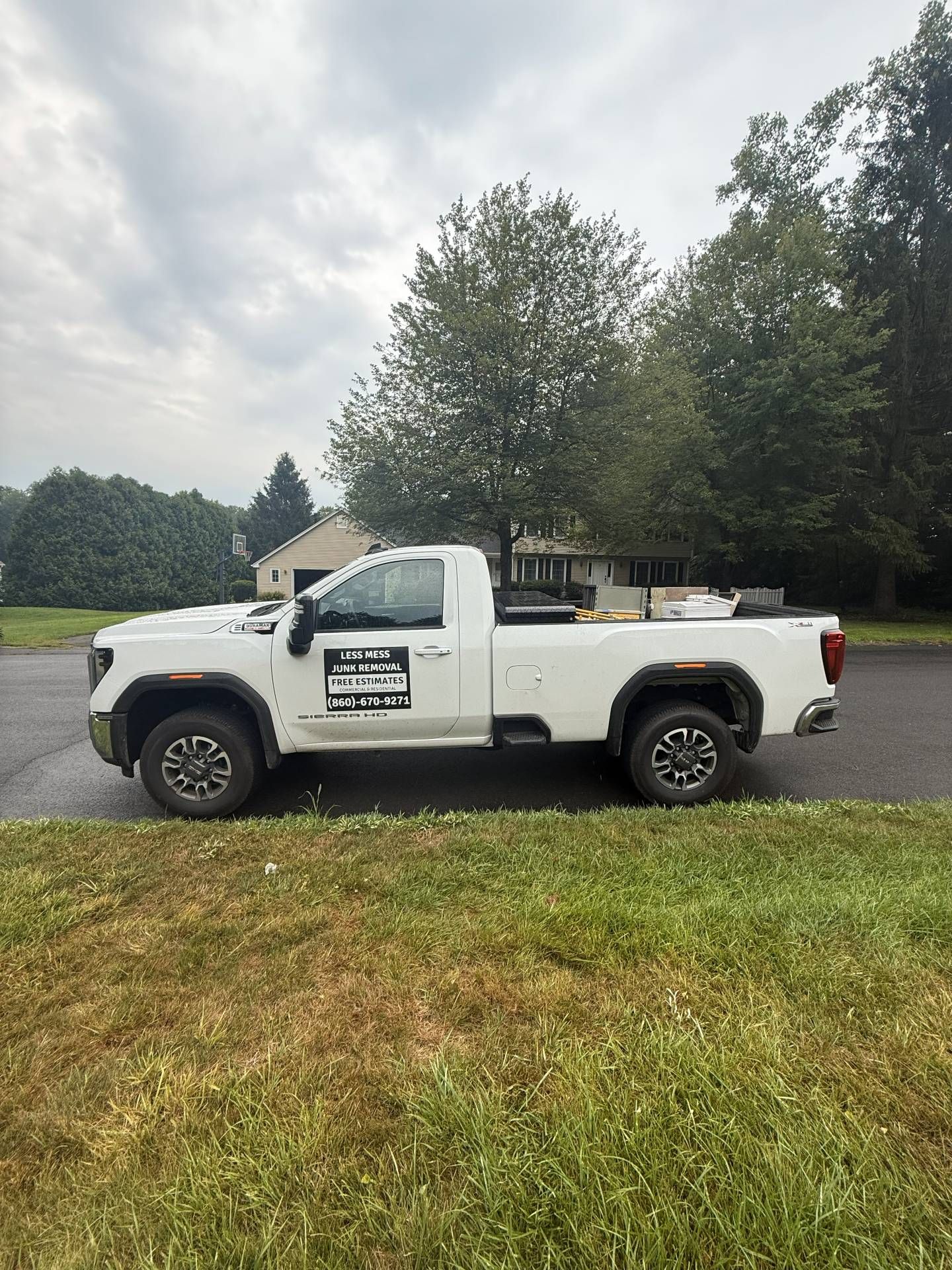 White pickup truck parked on grass, logo on door, trees and cloudy sky in the background.