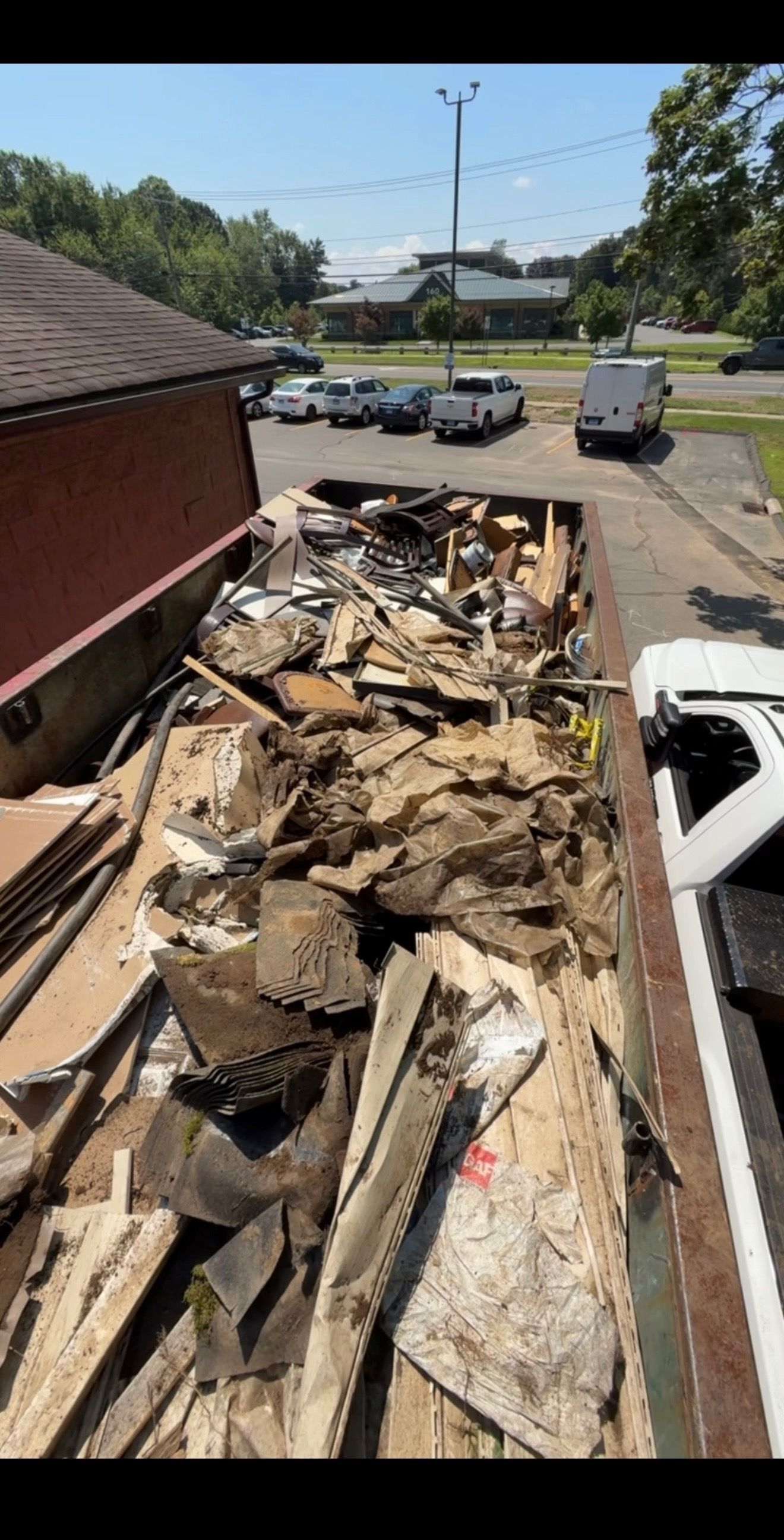 Dumpster filled with construction debris; vehicles and trees in background.