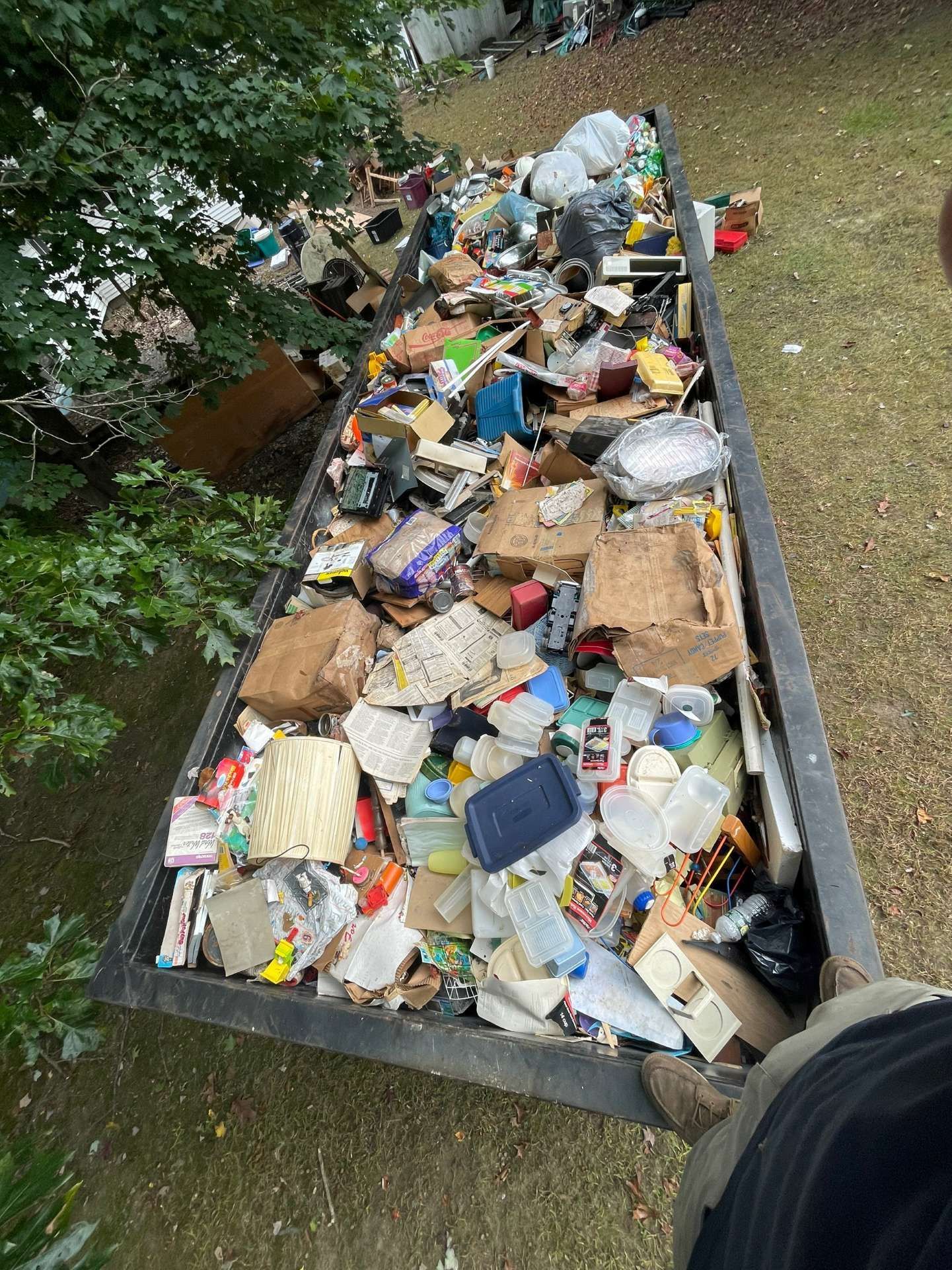 A dumpster overflowing with various trash and debris; outdoors.