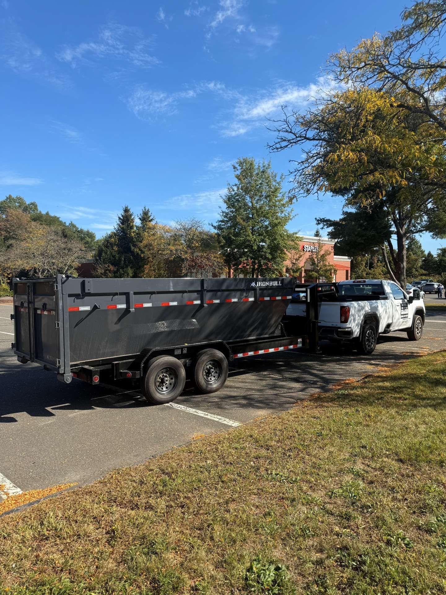 White truck towing a black dump trailer in a parking lot on a sunny day.
