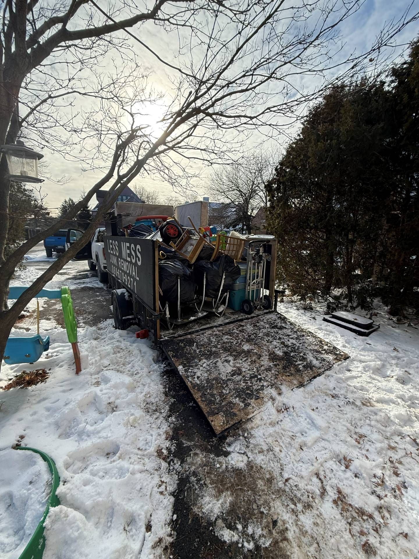 Open dumpster on snow-covered driveway, filled with items. Winter setting, bright sunlight.