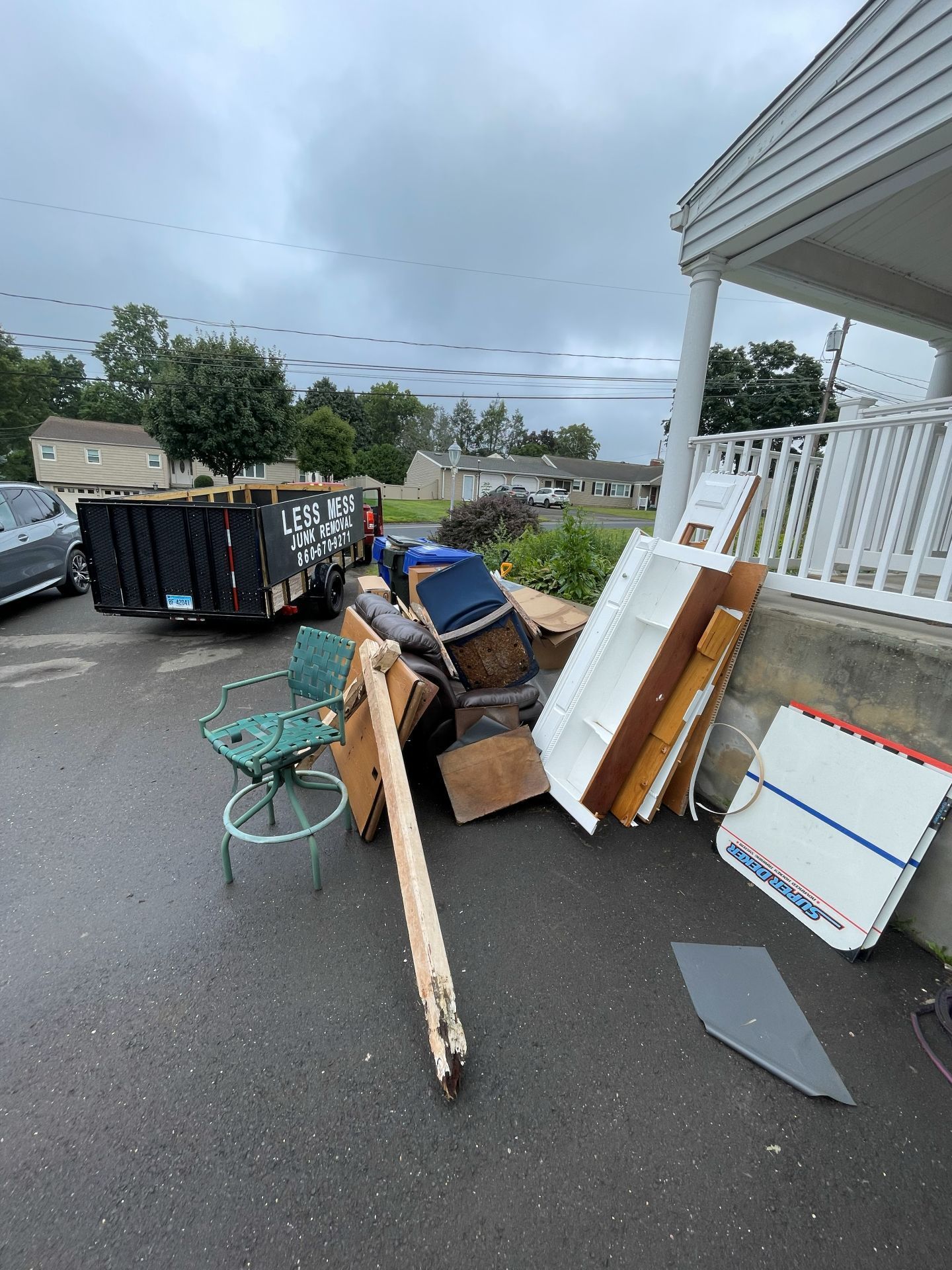 Pile of discarded furniture and debris next to a house with a dumpster in the background. Overcast day.