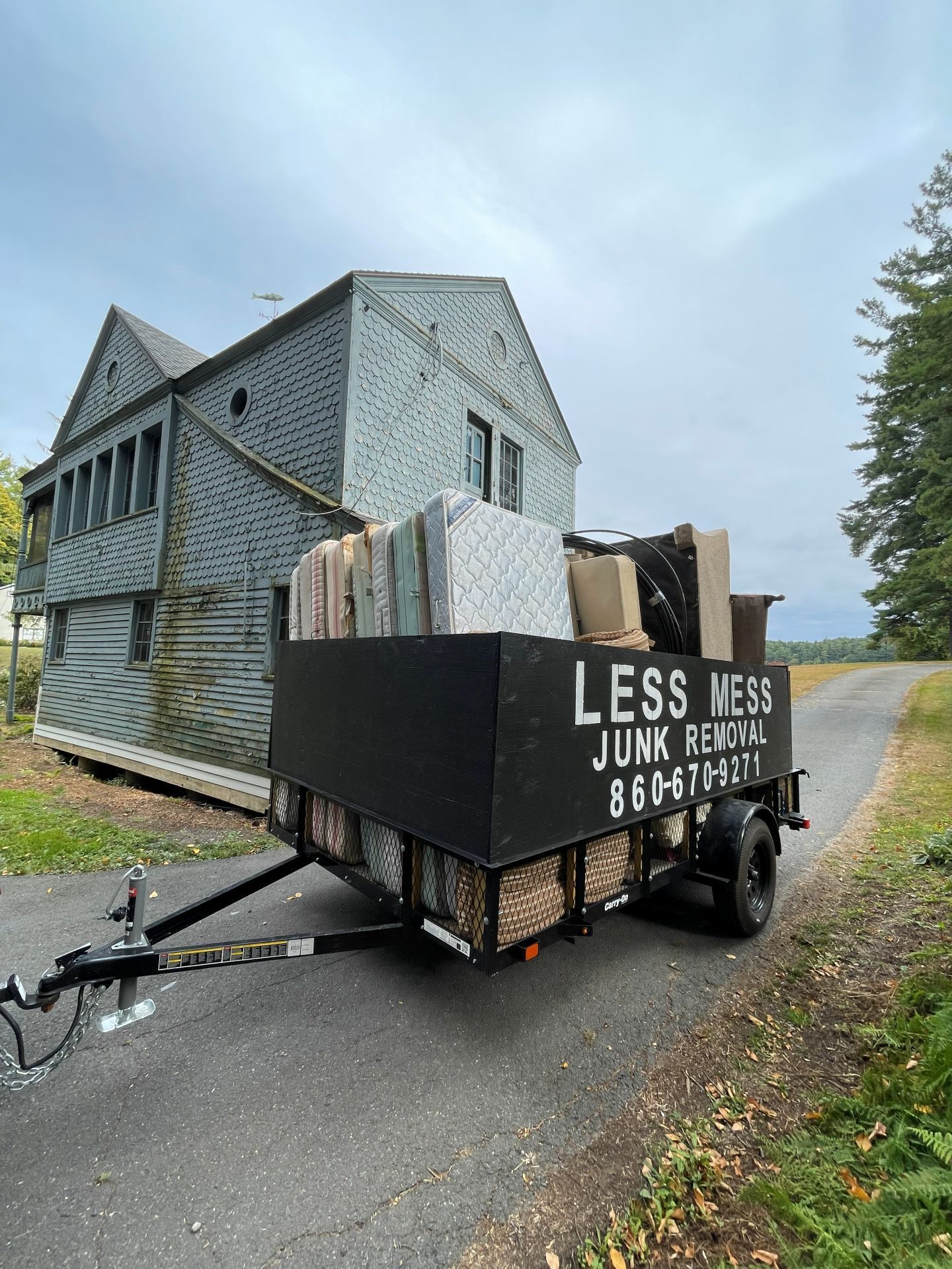 A trailer filled with junk in front of a weathered house; 