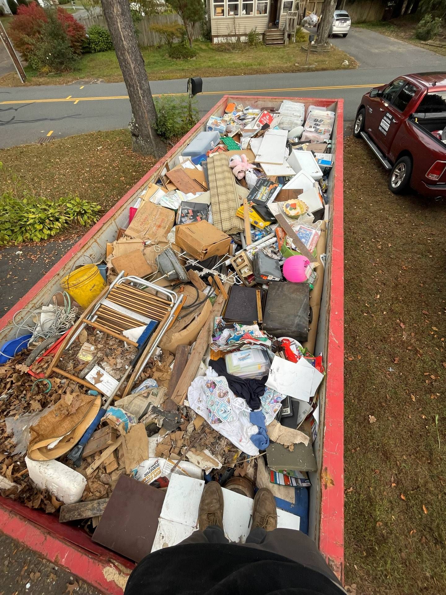 Dumpster filled with household debris, set in a residential area. Red container, various trash items.