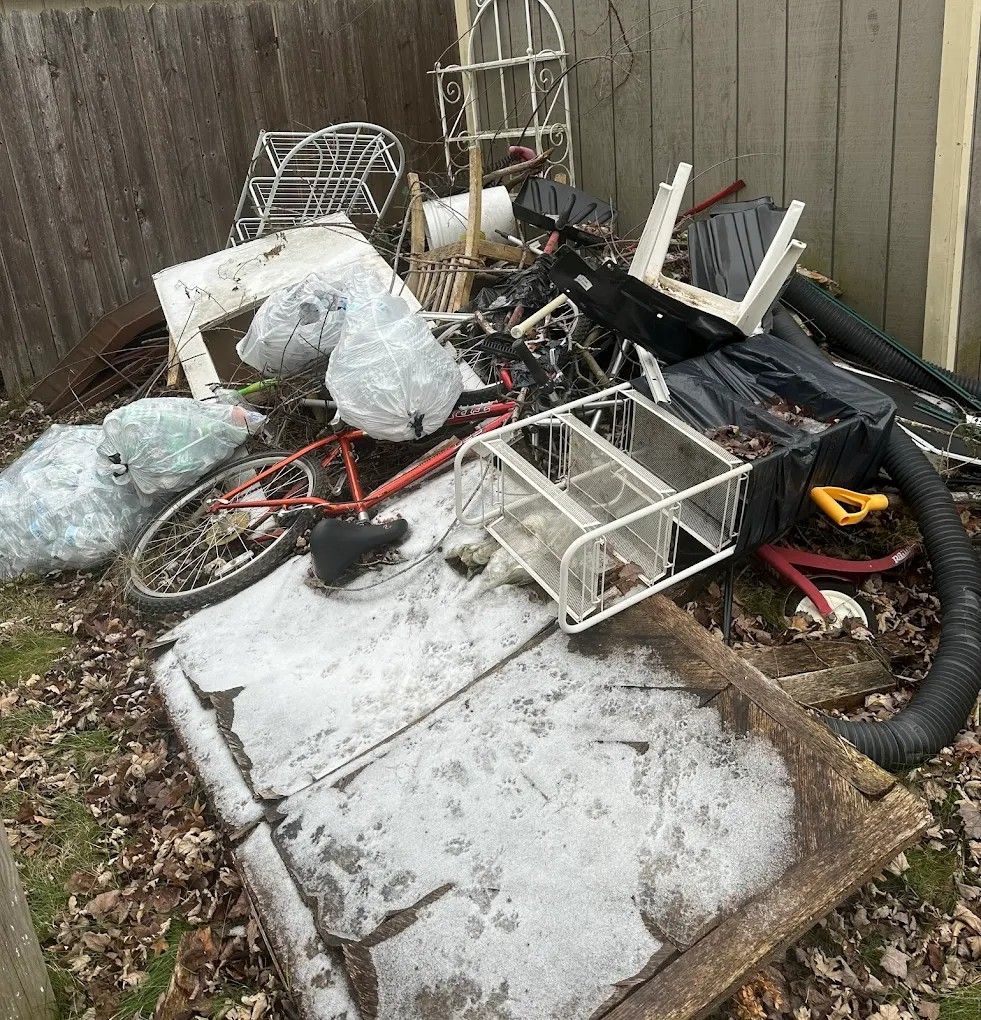 Pile of assorted junk, including a bike, furniture, and bags, in a yard.