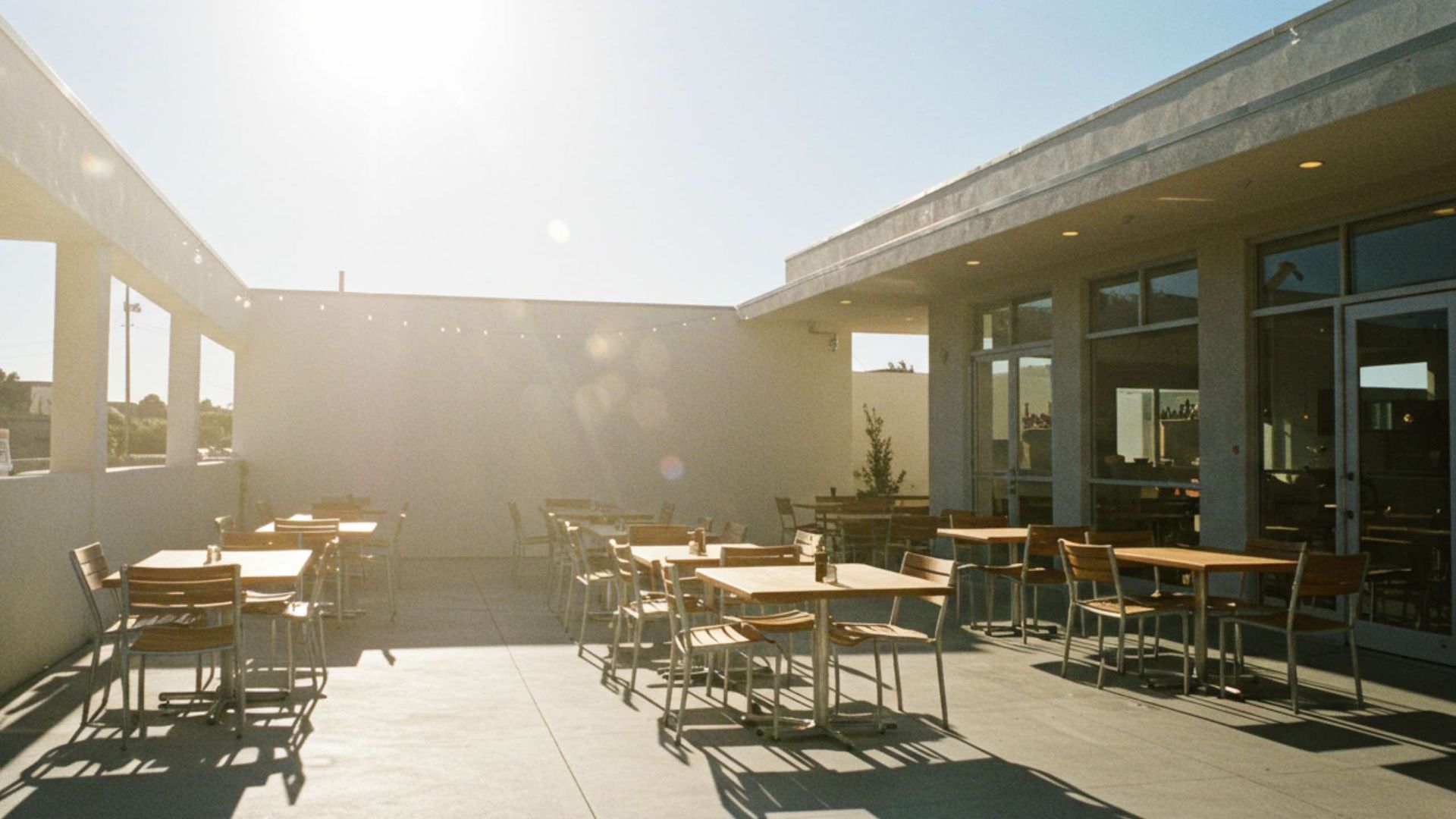 Outdoor patio with tables and chairs, sunny setting, neutral building colors.