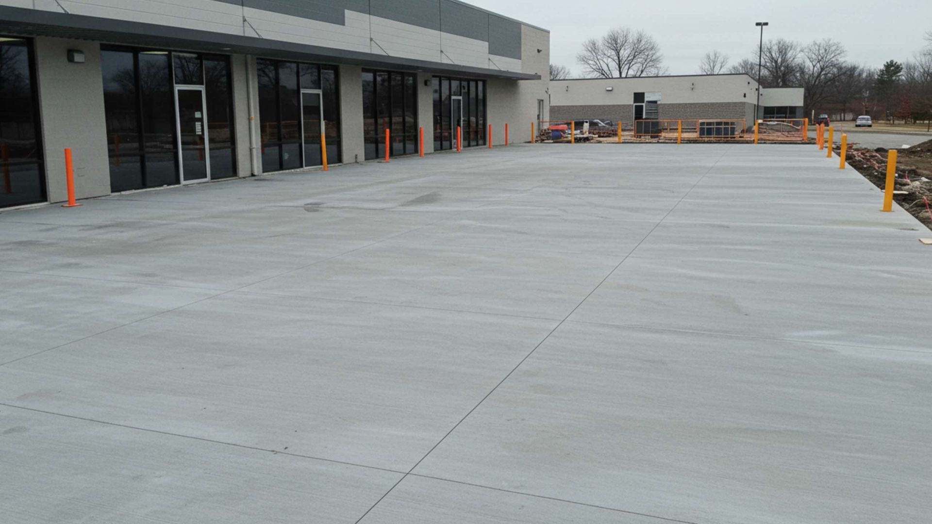 Newly poured concrete storefront patio, gray, with orange and yellow safety posts.