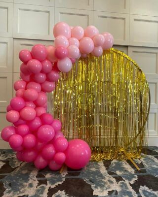 A bunch of pink balloons are sitting in front of a gold curtain.