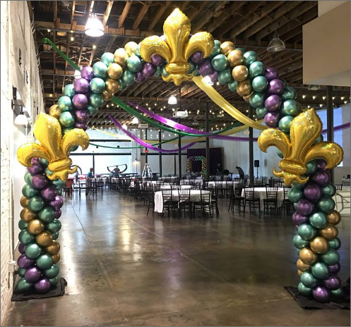 A large room filled with tables and chairs decorated with mardi gras balloons.