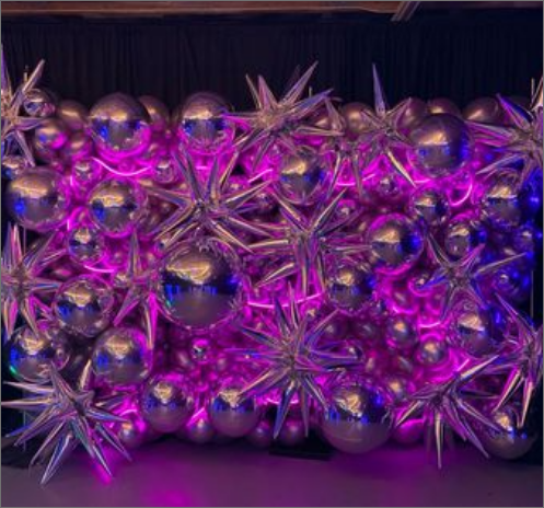 A wall of silver balloons with purple lights behind them.