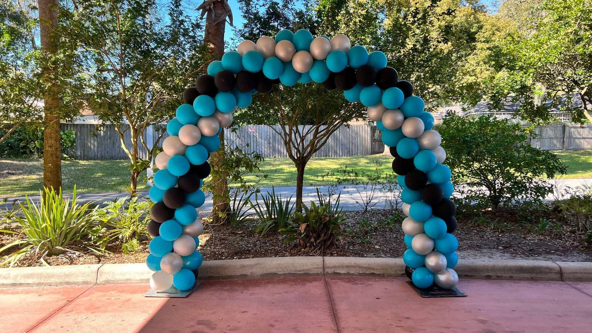A blue , black , and silver balloon arch is sitting on a sidewalk.