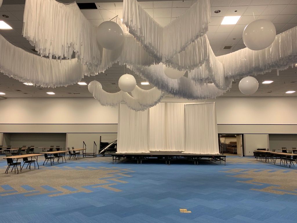 A large room with tables and chairs and balloons hanging from the ceiling.