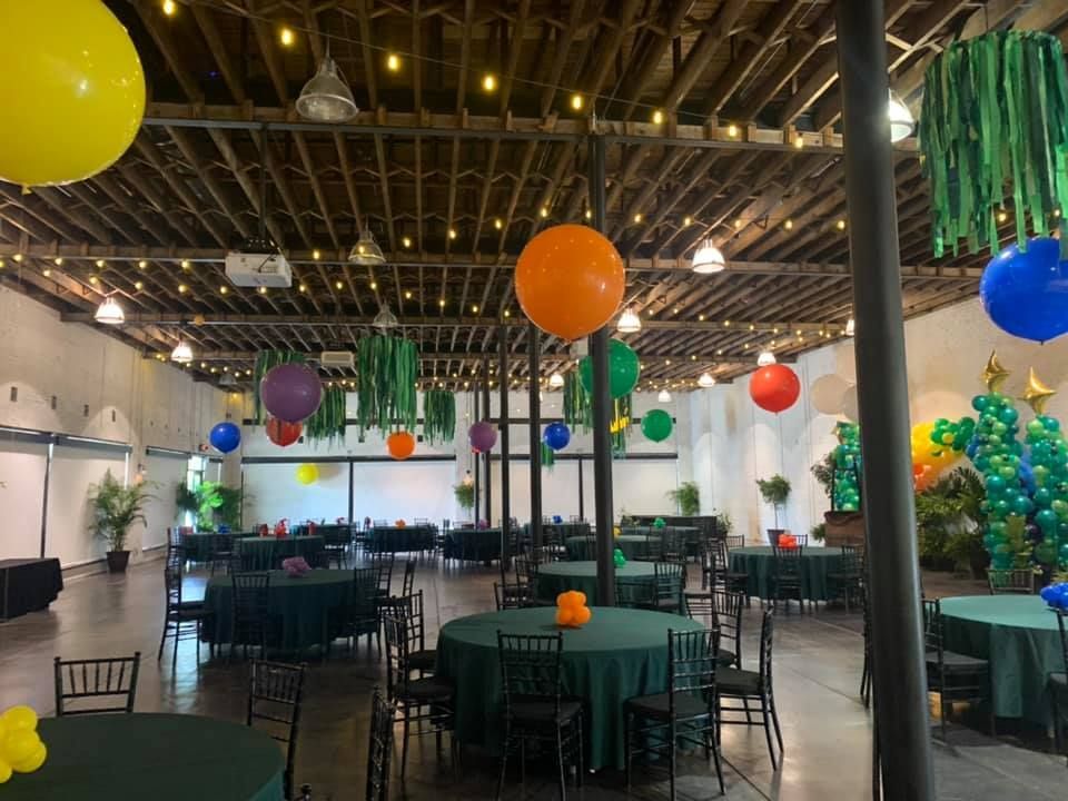 A large room with tables and chairs and balloons hanging from the ceiling.