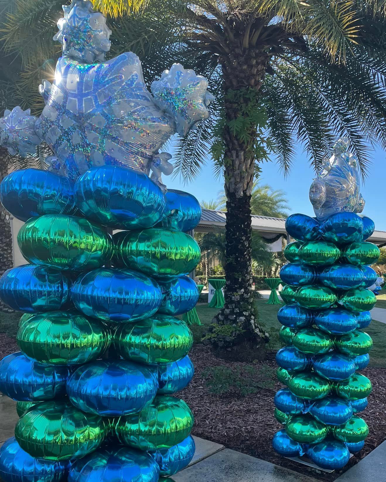 A bunch of blue and green balloons stacked on top of each other in front of a palm tree.