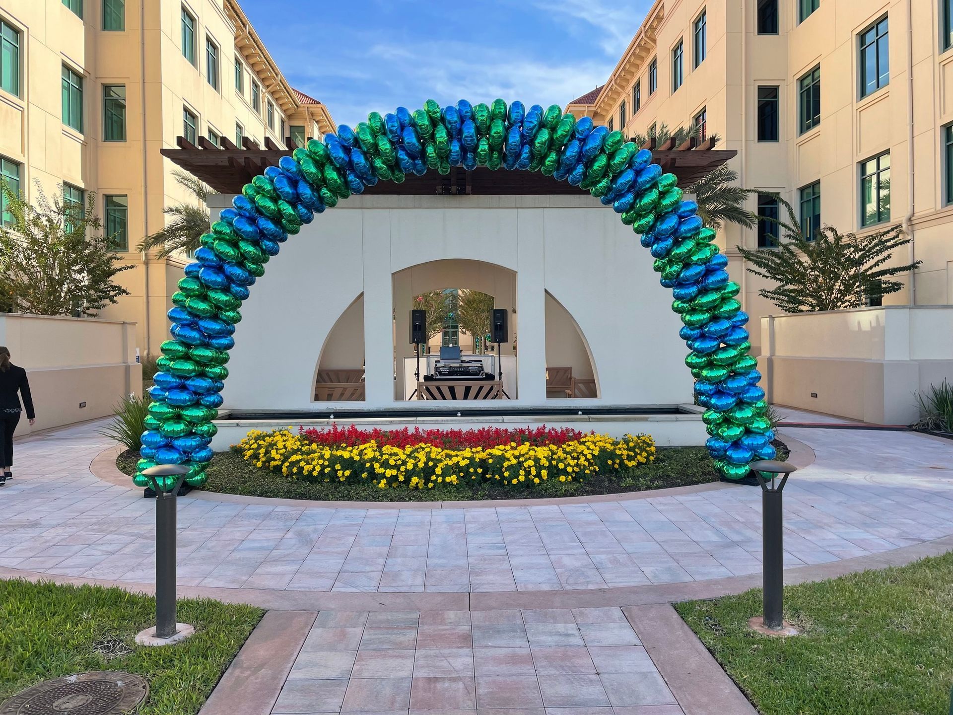 A large arch made of blue and green balloons is in front of a building.
