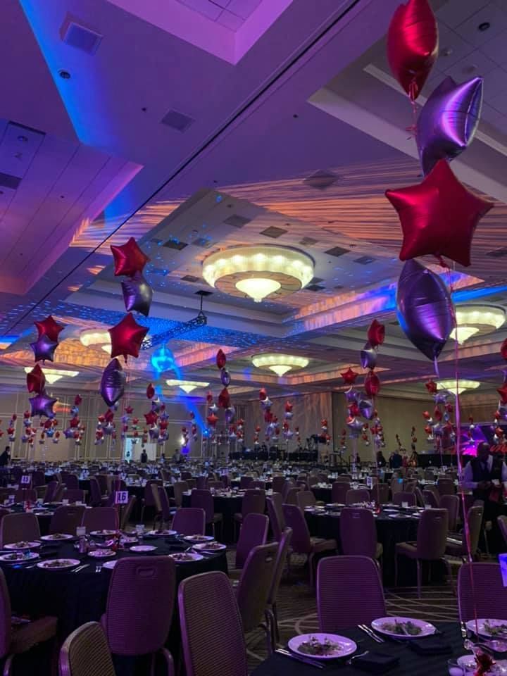 A large room with tables and chairs and balloons hanging from the ceiling.