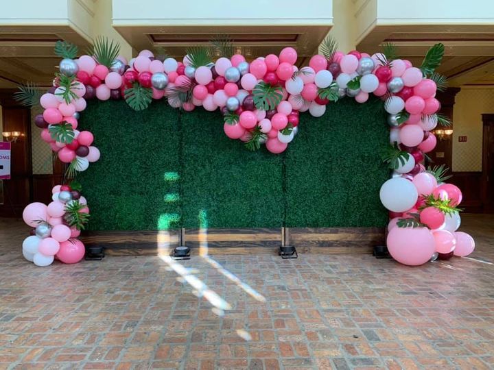 A wall covered in pink and white balloons and flowers.