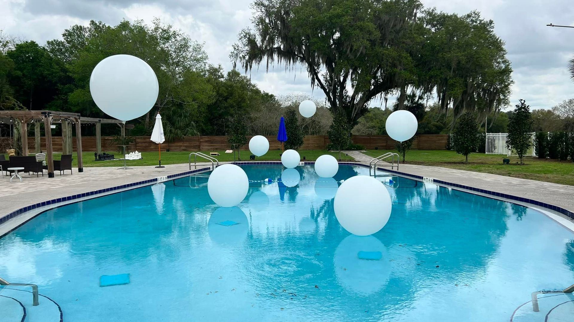 A swimming pool decorated with white balloons and trees in the background.