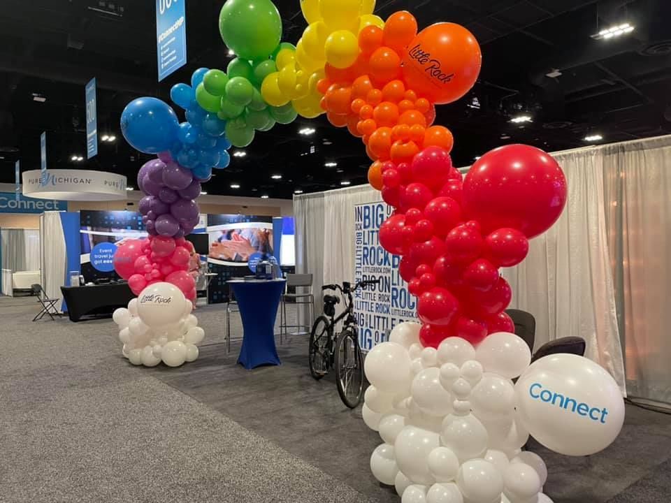 A rainbow made of balloons in a room with a bicycle in the background.