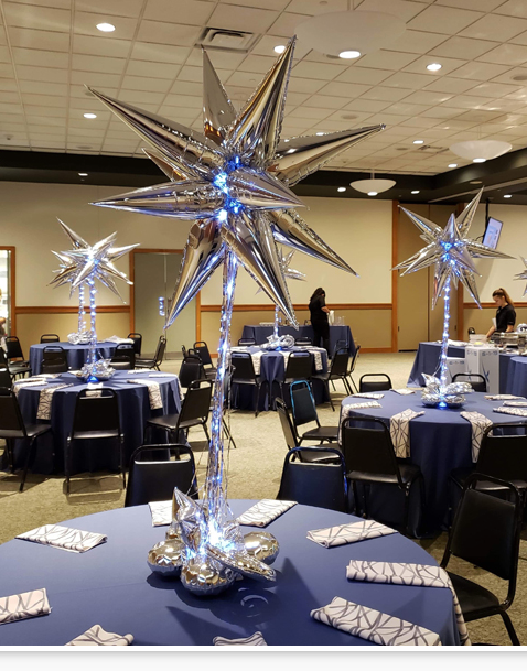 A room filled with tables and chairs with silver star centerpieces