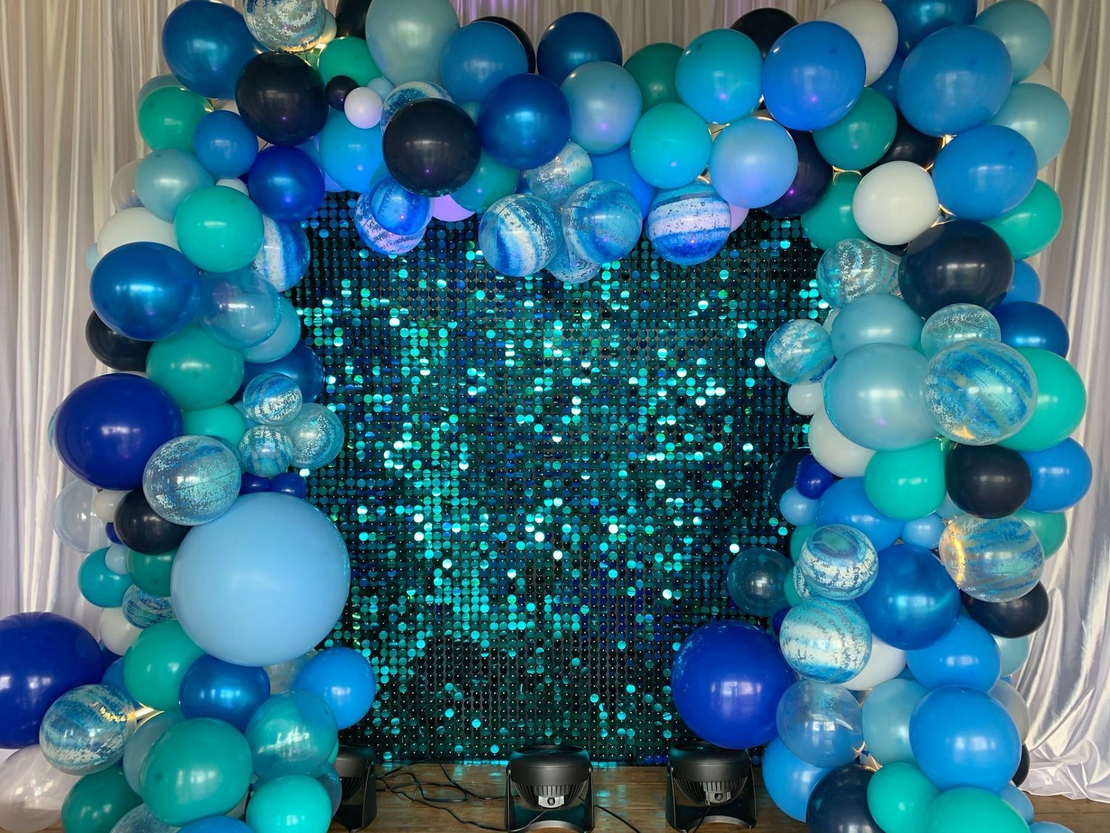 A bunch of blue balloons are sitting in front of a sequined wall.
