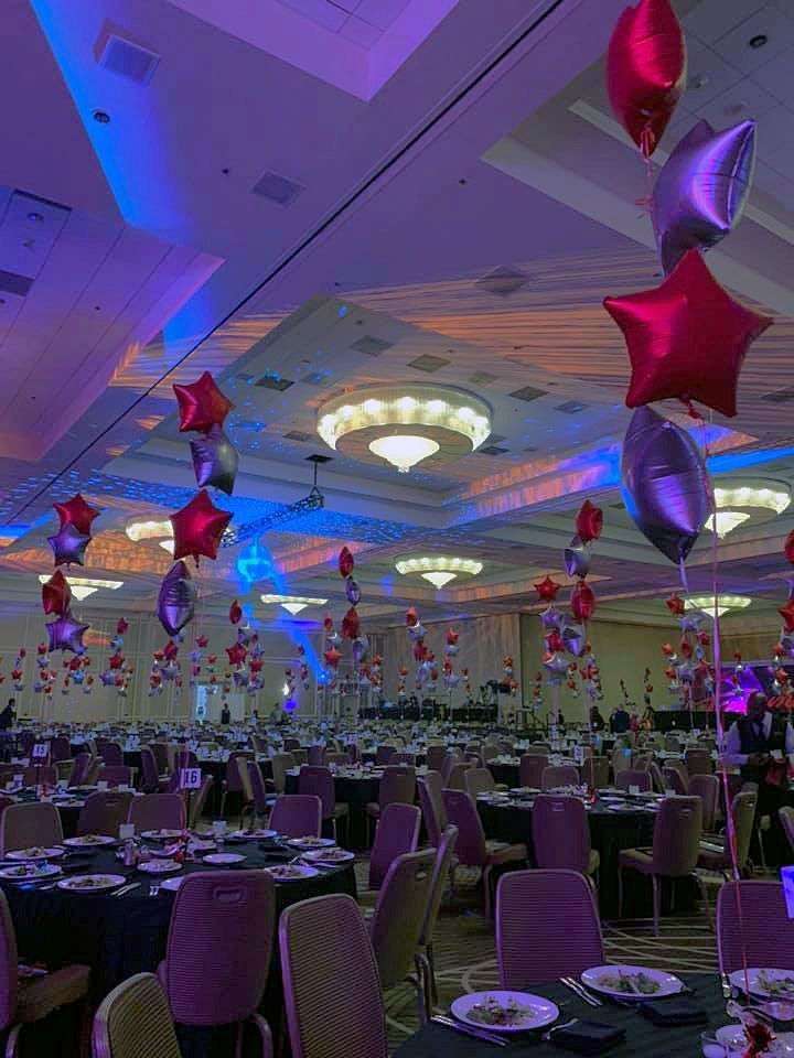 A large room with tables and chairs and balloons hanging from the ceiling.