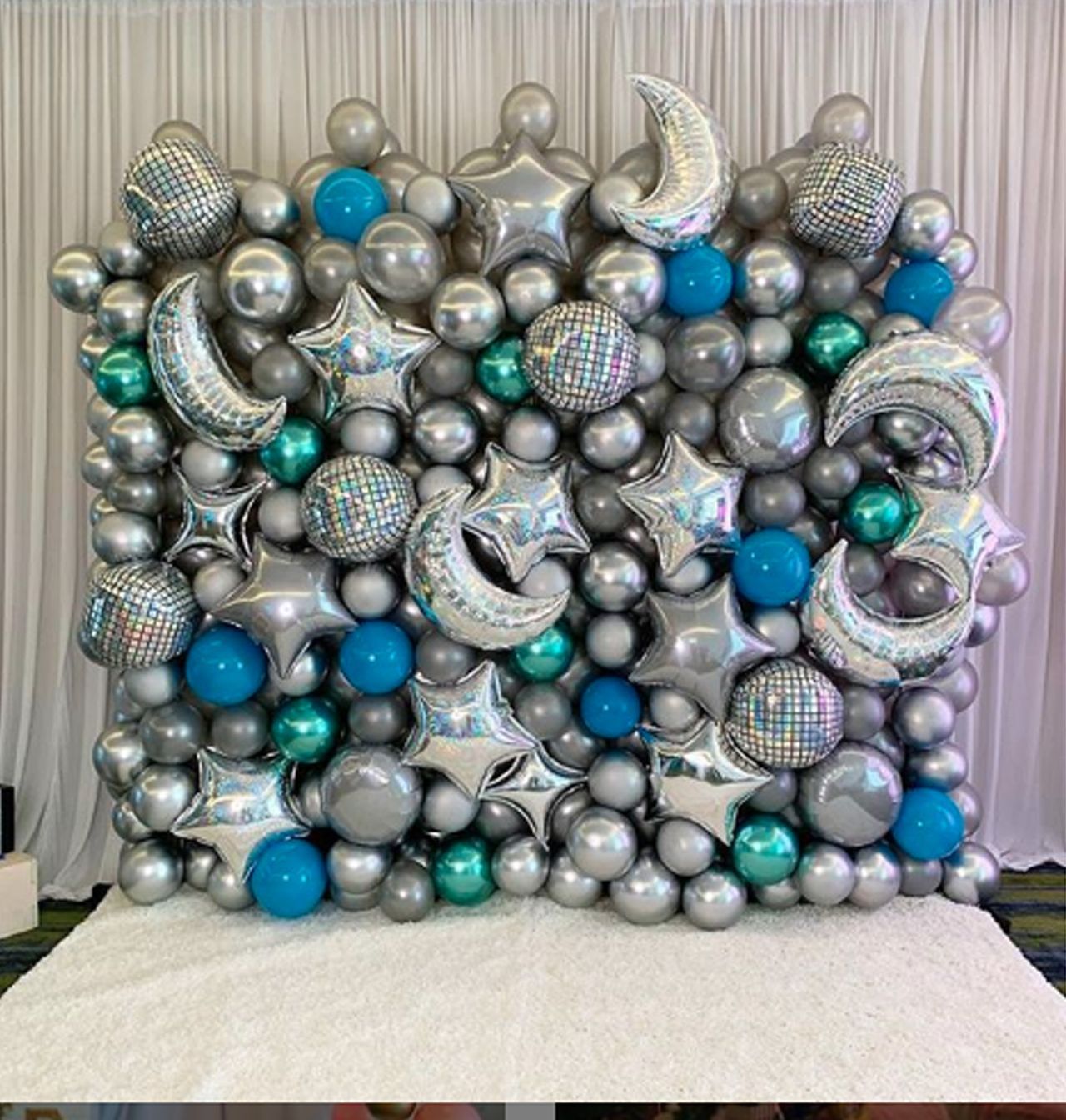A wall of balloons with a white curtain behind it.