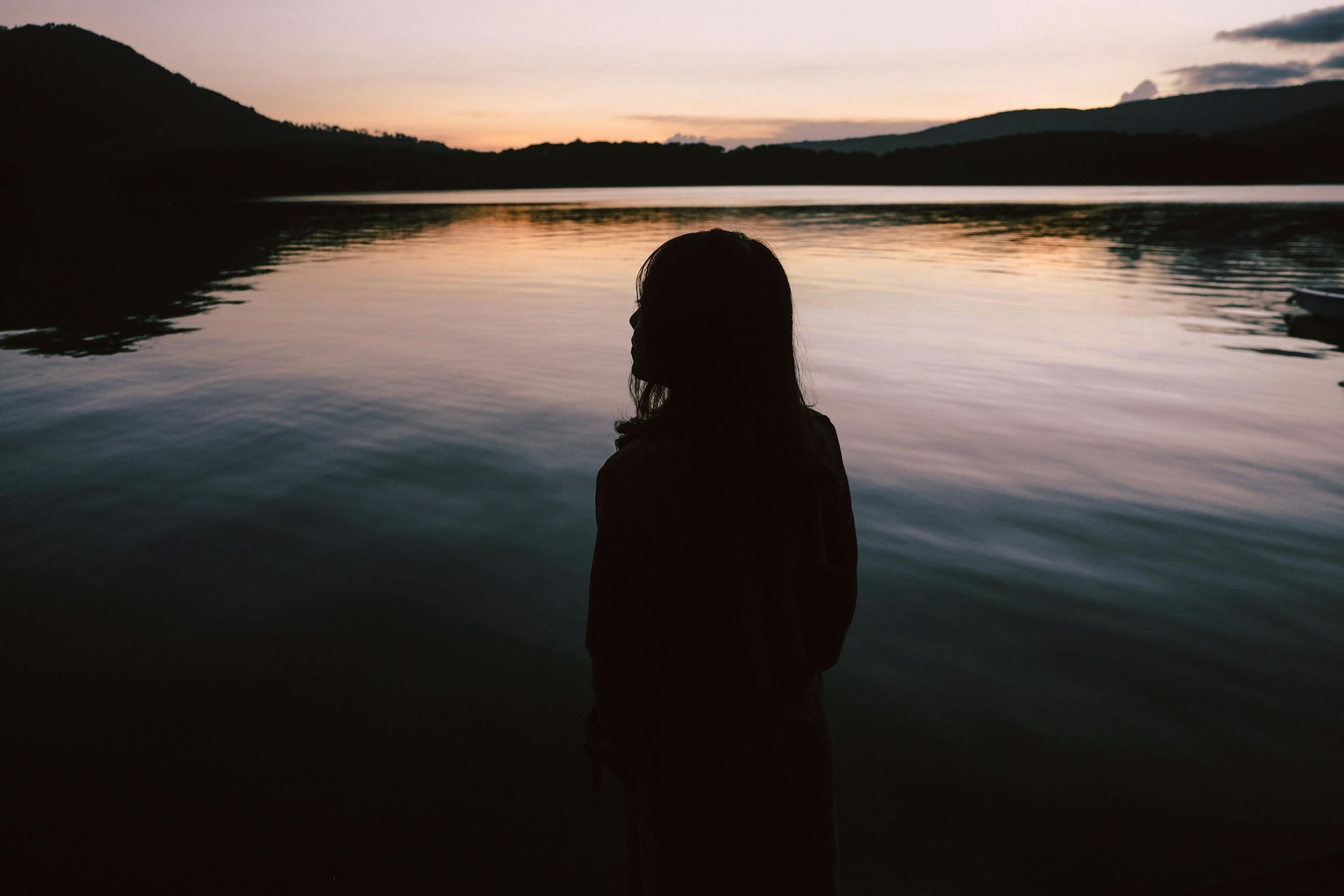 A woman is standing in front of a lake at sunset.