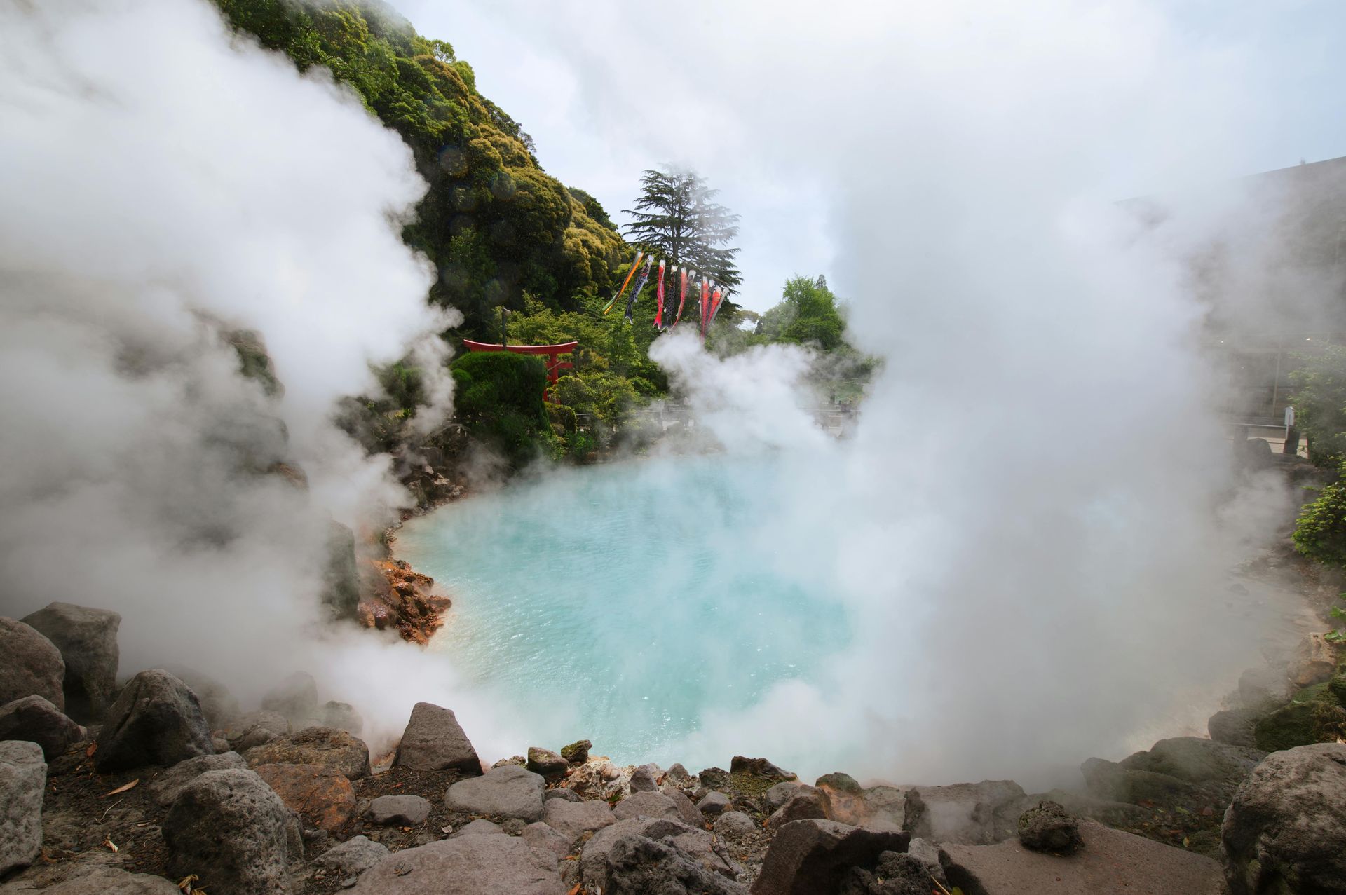 Azure-colored hot spring surrounded by rocks, releasing thick white steam in Japan.
