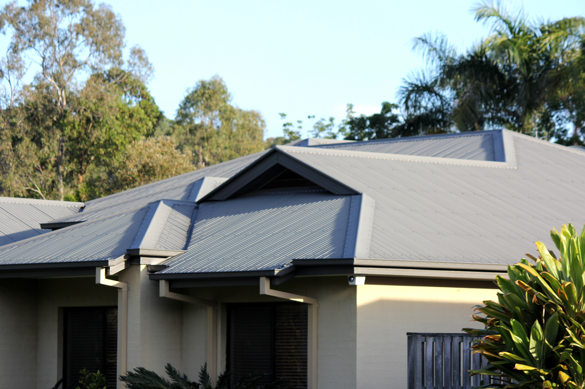 Gray metal roof on a beige house with trees in the background.