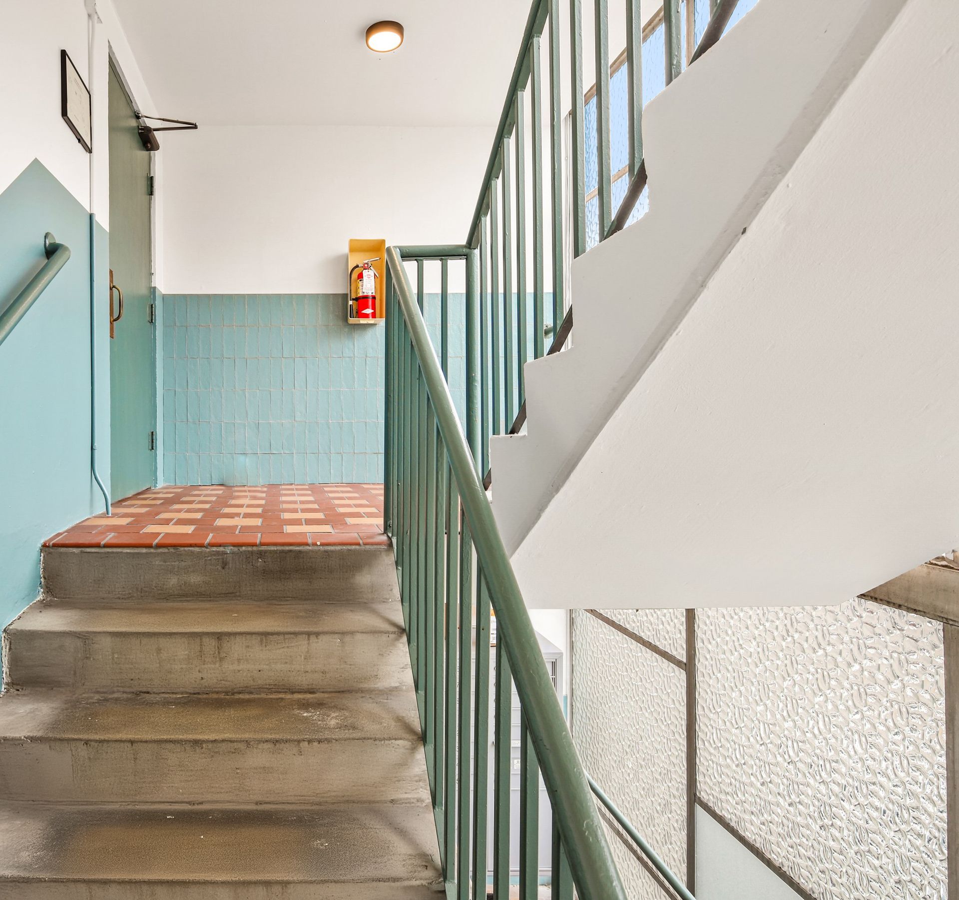 A staircase with a green railing and a fire extinguisher on the wall