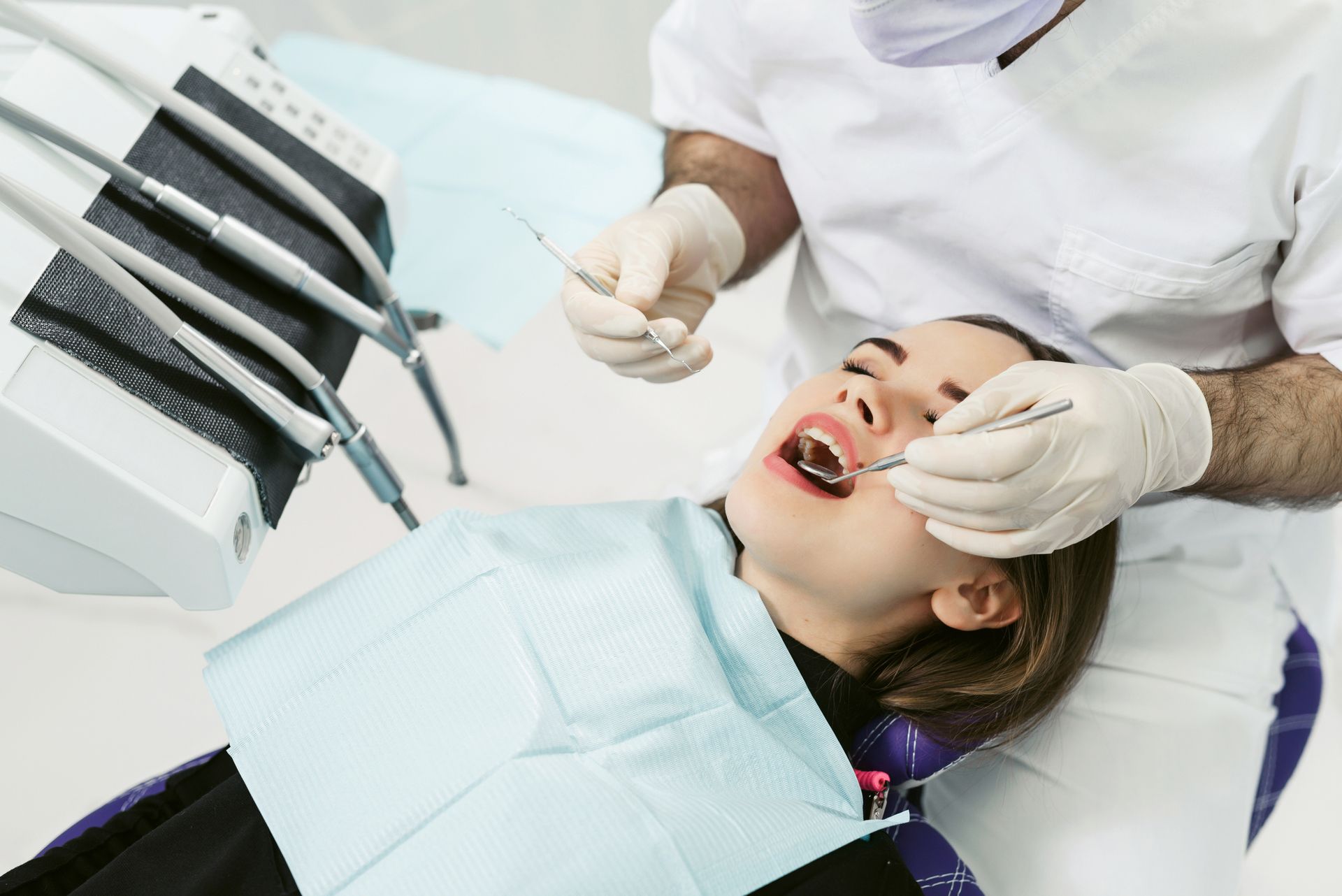 Dentist examining patient's teeth with tools in a dental office.