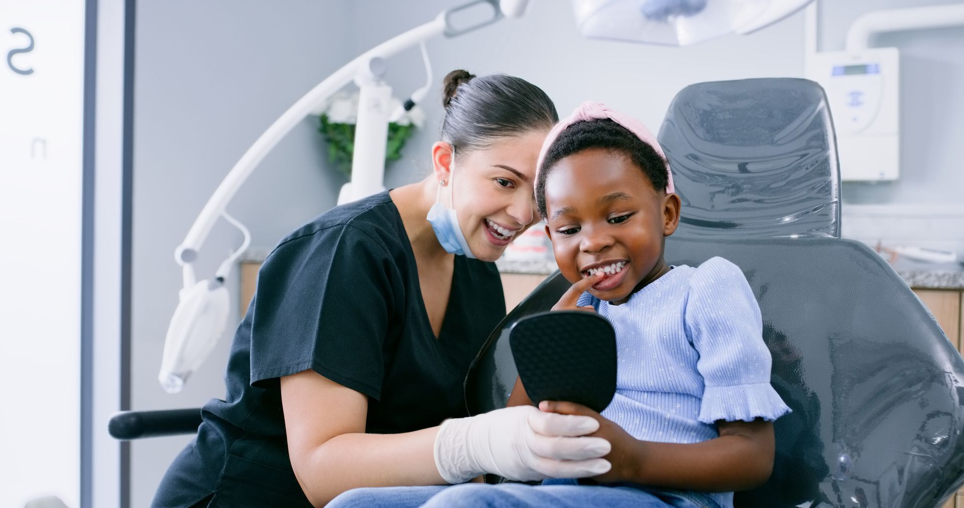 Dentist and young patient looking at teeth in a hand mirror; dental chair setting.