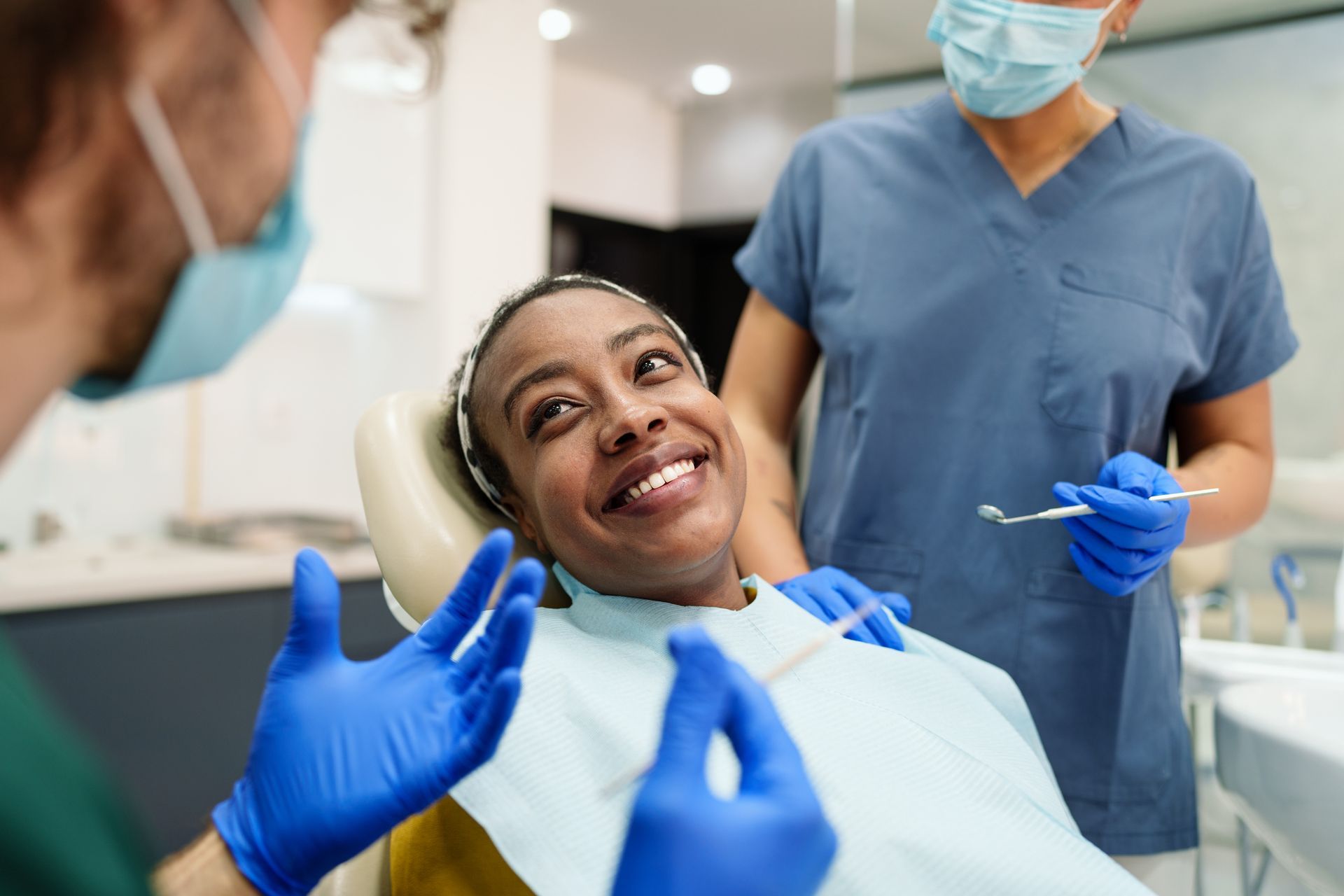 Patient smiles in dentist's chair while dentist and assistant wear masks and gloves.