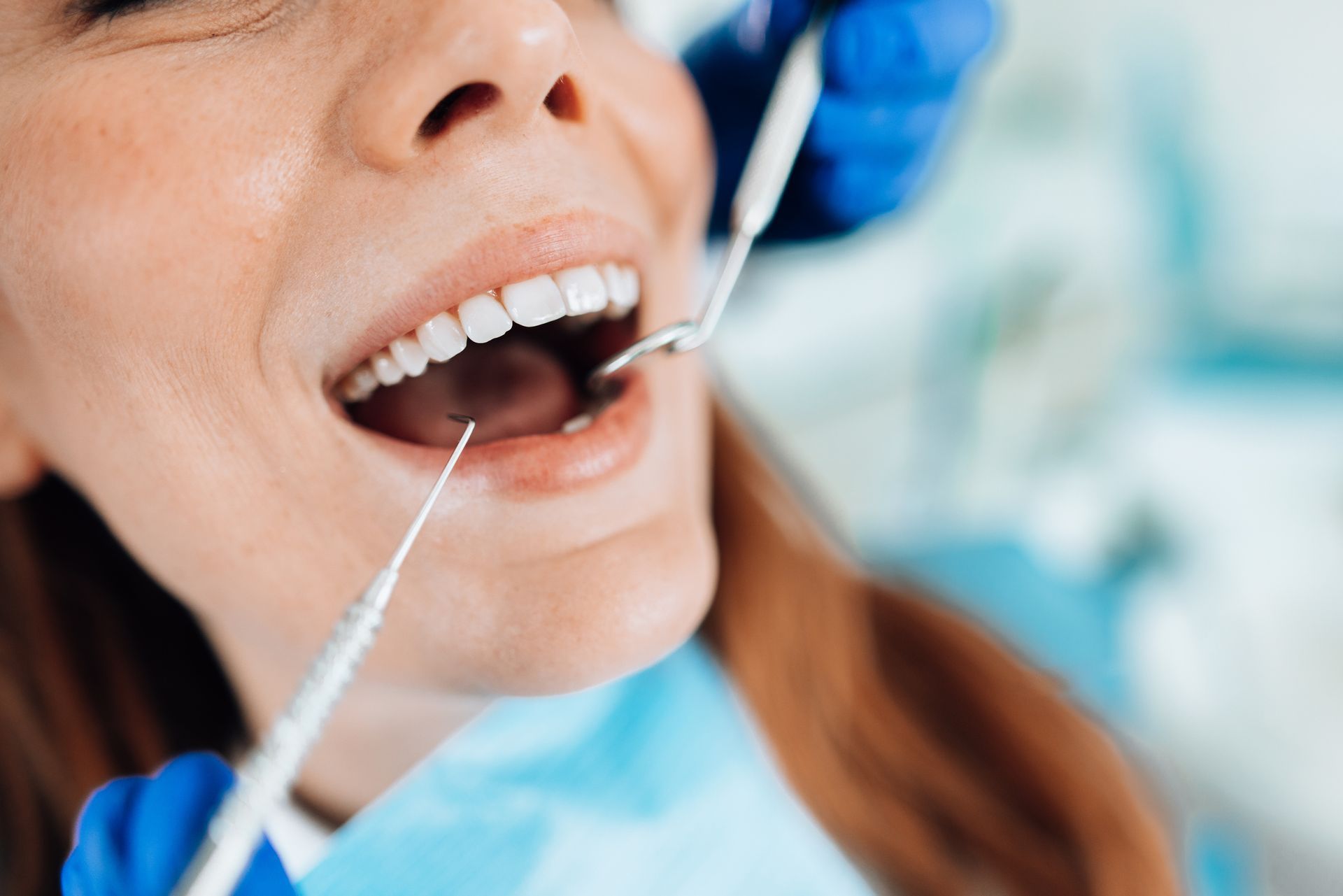 Woman at dentist's appointment, mouth open as dental tools are used.