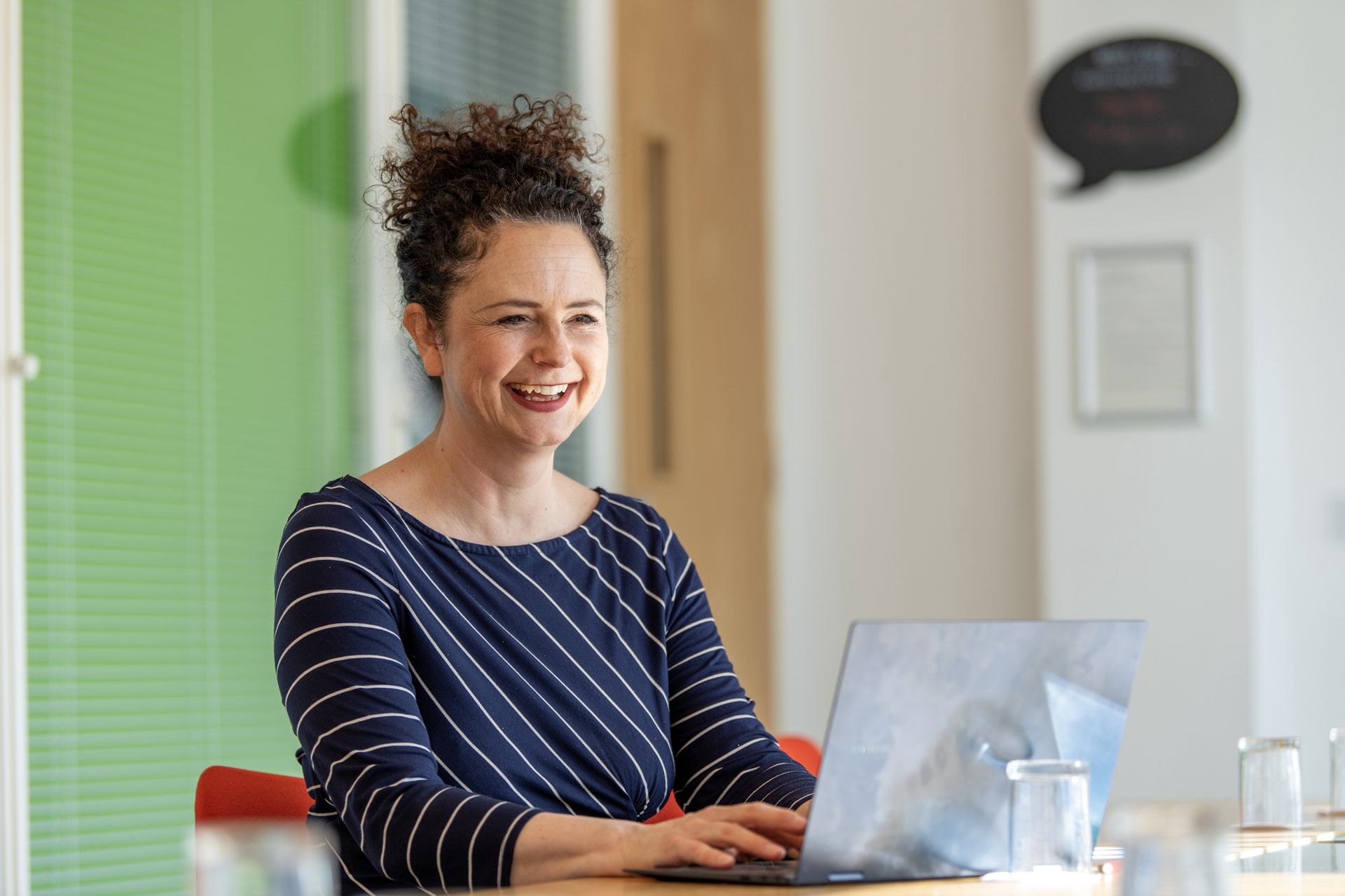 Kay is sitting at a table using a laptop computer.