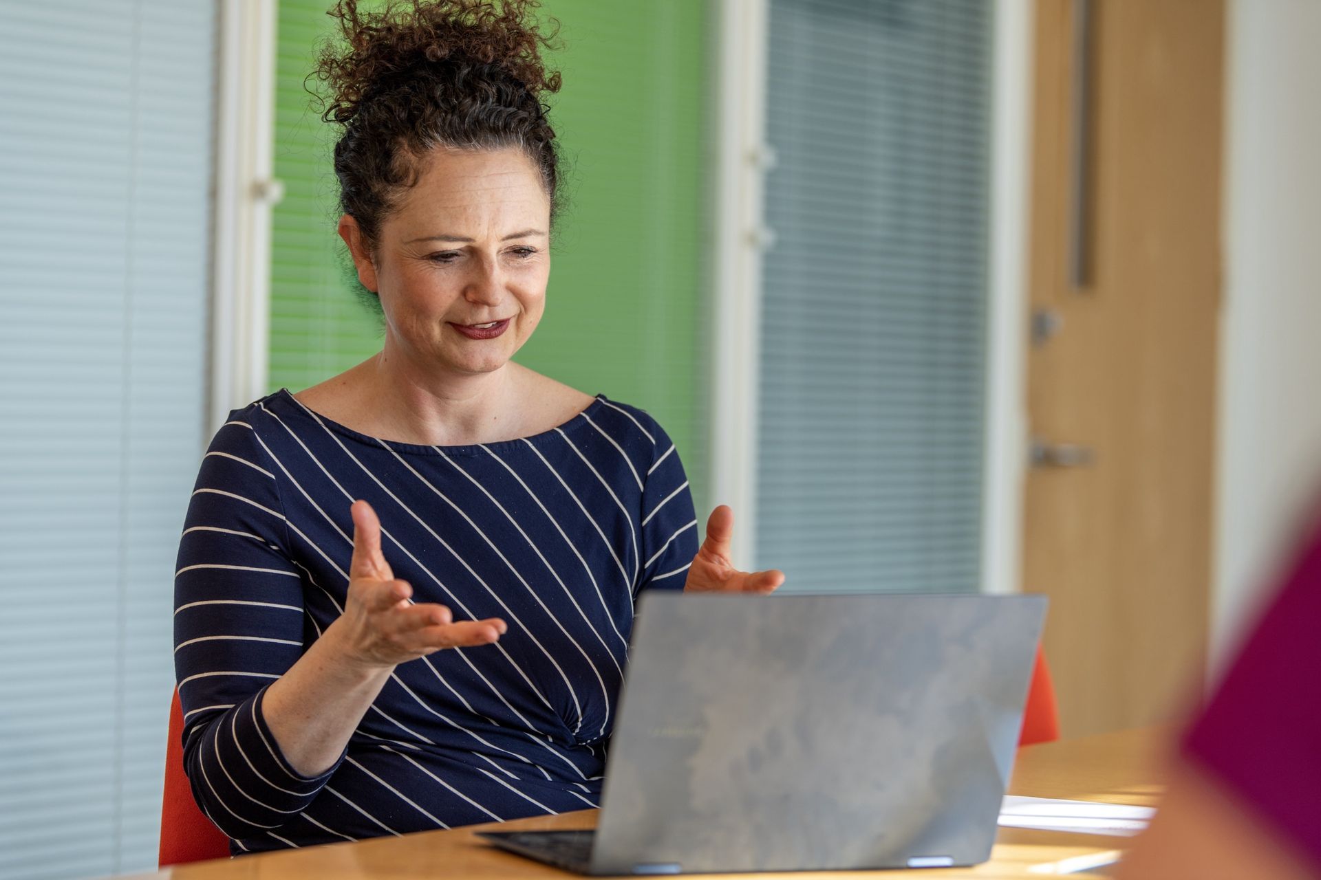 Kay is sitting at a table using a laptop computer.